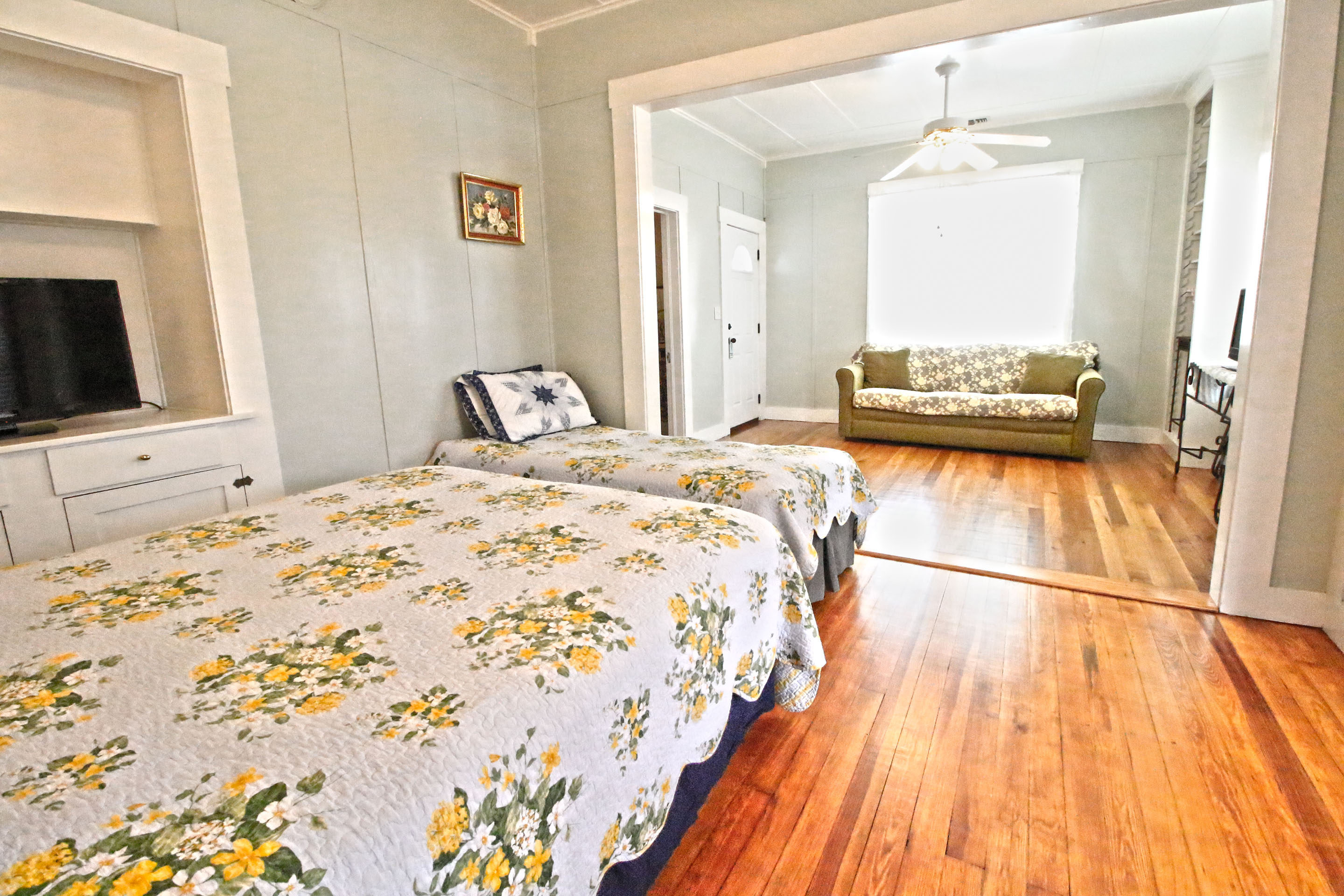 A suite with two beds, a sofa, and a TV in a room with hardwood floors and a doorway to another area.
