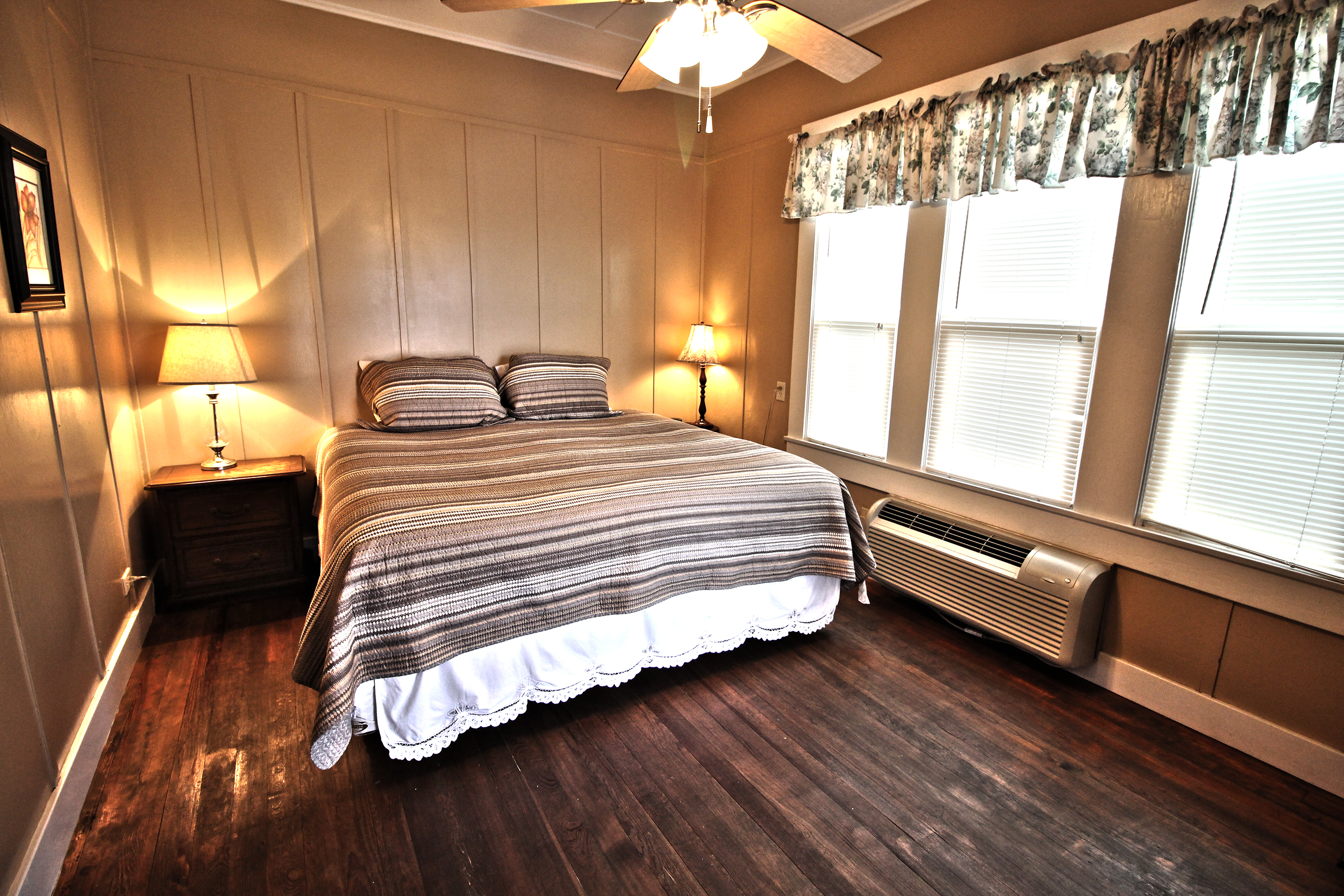 A wide view of a hotel room with a bed, nightstand, lamps, and a window.