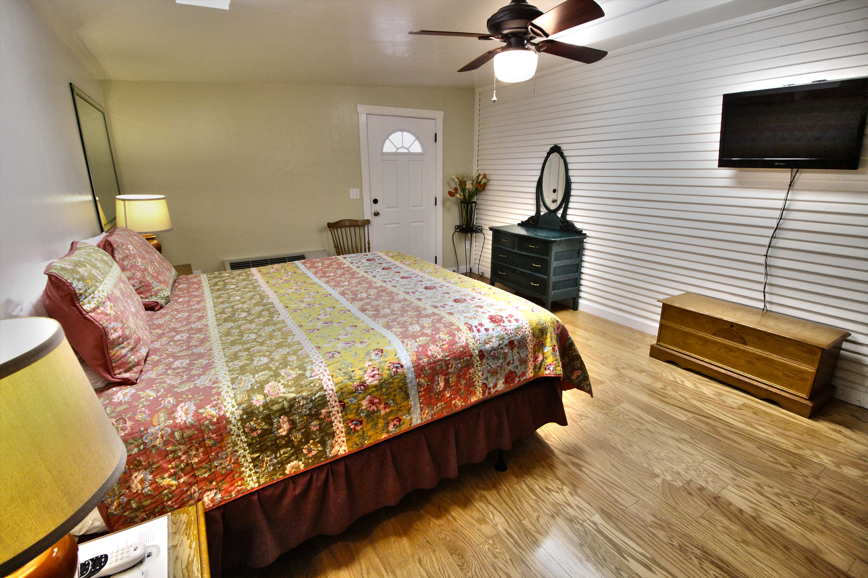 A wide-angle view of a hotel room with a bed, TV, dresser, and lamp.