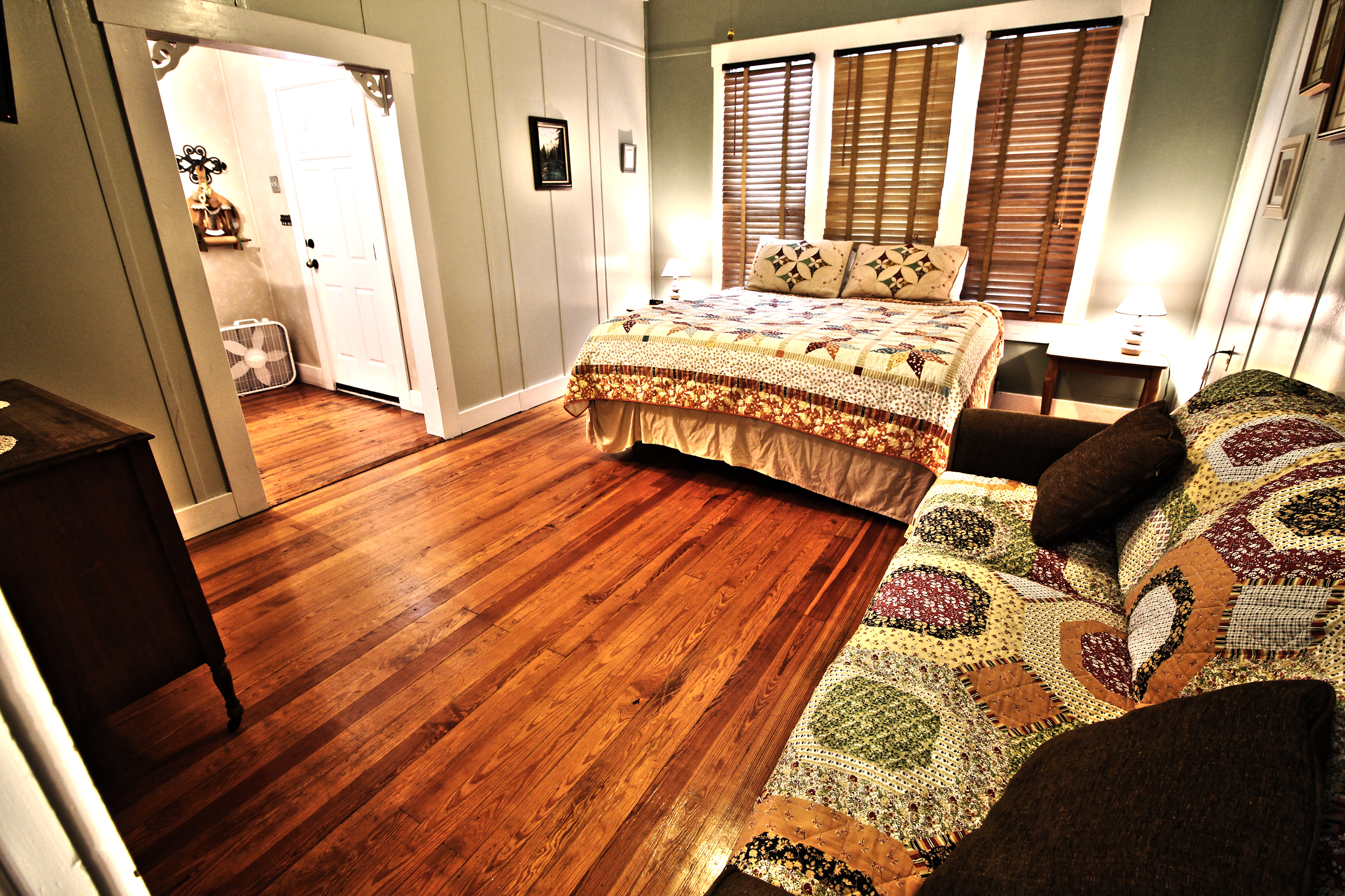 A wide-angle view of a room with a bed, sofa, and doorway.