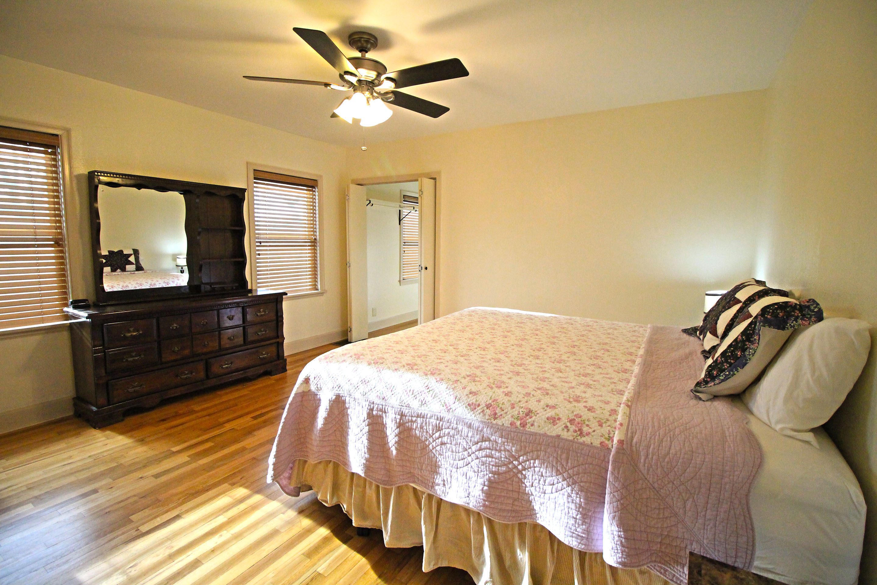 A wide view of a guest room with a bed, dresser, and ceiling fan.