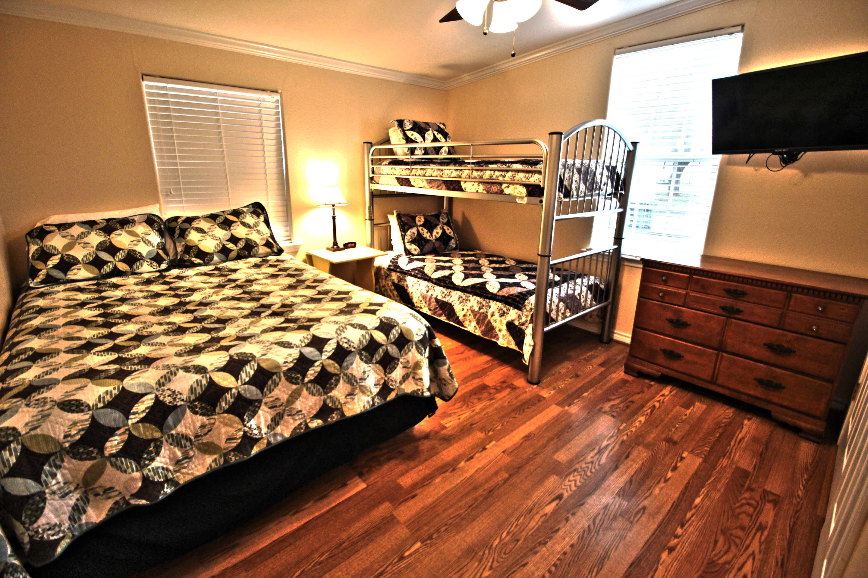 A hotel room with a queen bed, bunk bed, dresser, and TV
