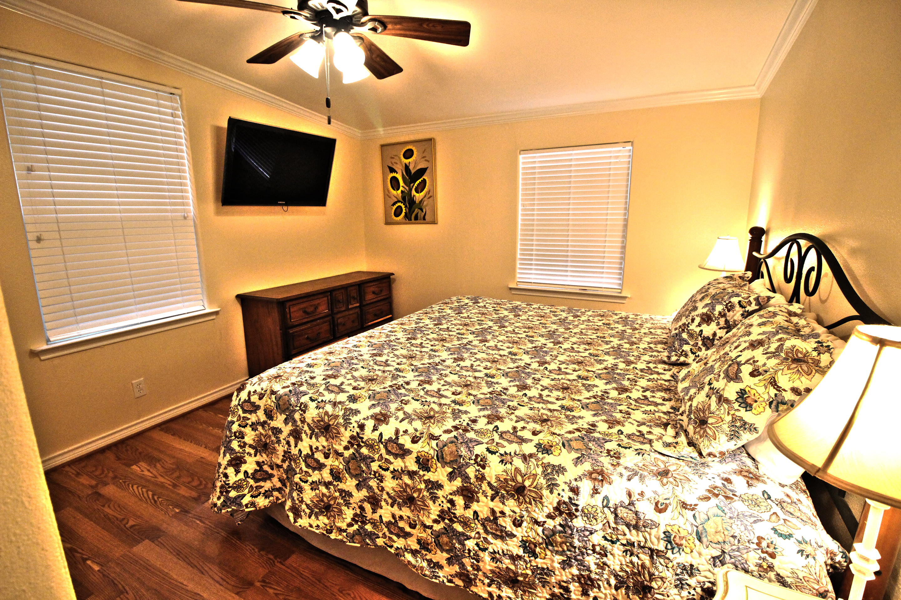 A wide-angle view of a hotel room with a bed, TV, dresser, and lamp.