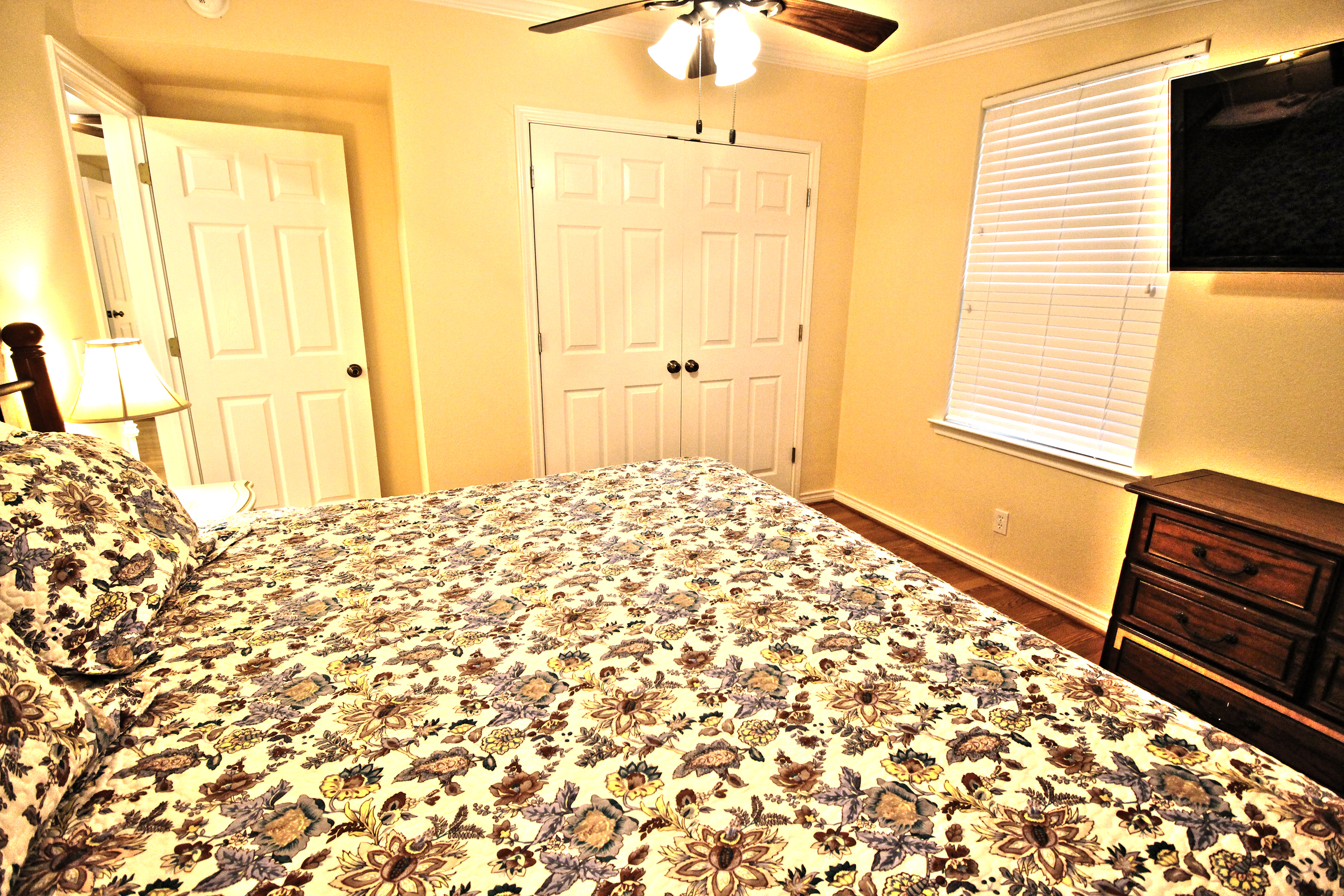 A wide view of a hotel room with a bed, dresser, TV, and window.