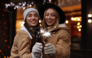 Two girls stand, slightly blurred, holding sparklers, which are in focus, celebrating the New Year in Fredericksburg, TX.