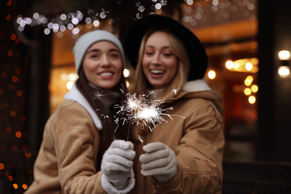 Two girls stand, slightly blurred, holding sparklers, which are in focus, celebrating the New Year in Fredericksburg, TX.